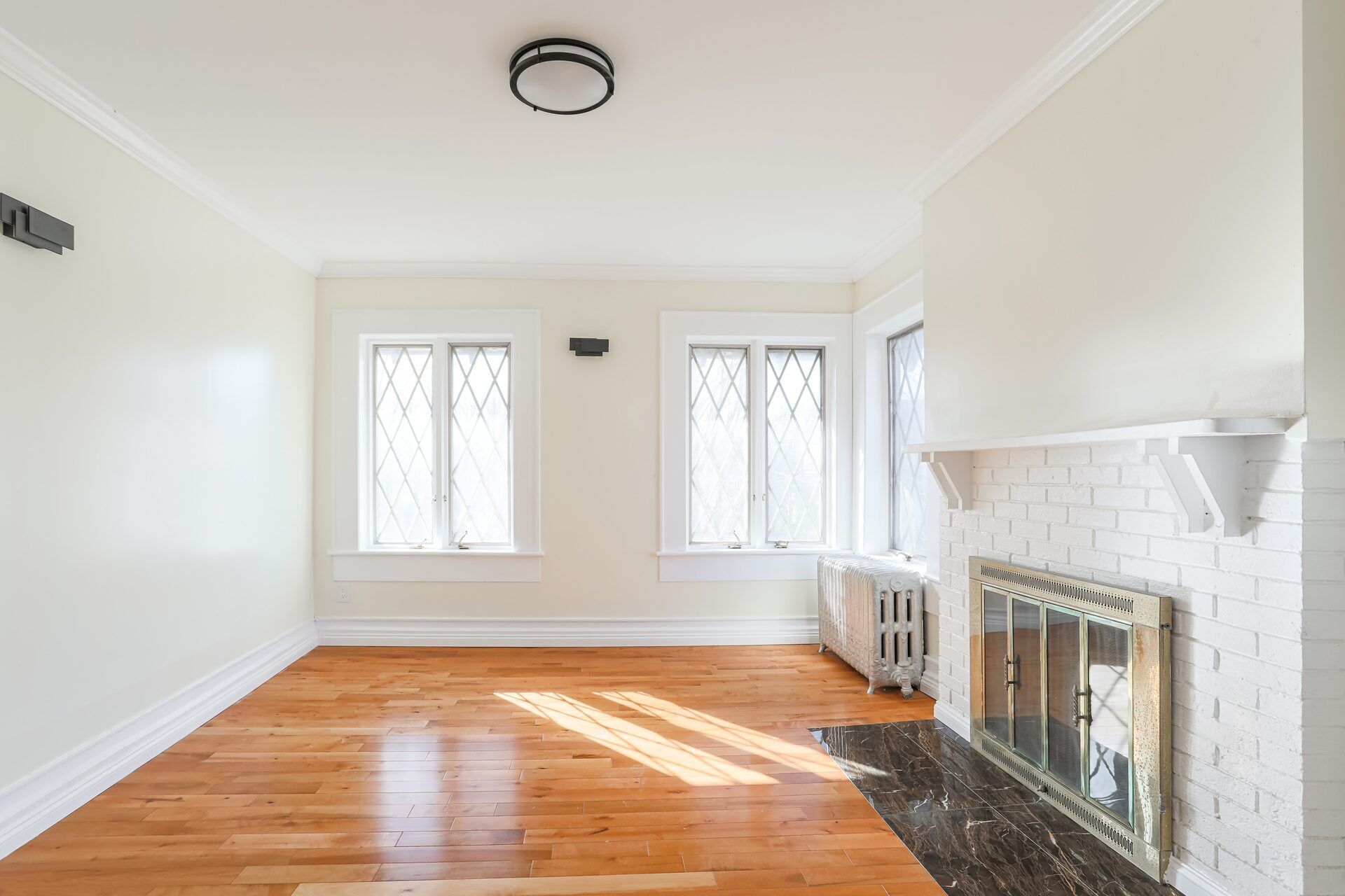 Empty living room with hardwood floors, a white brick fireplace, and leaded glass windows