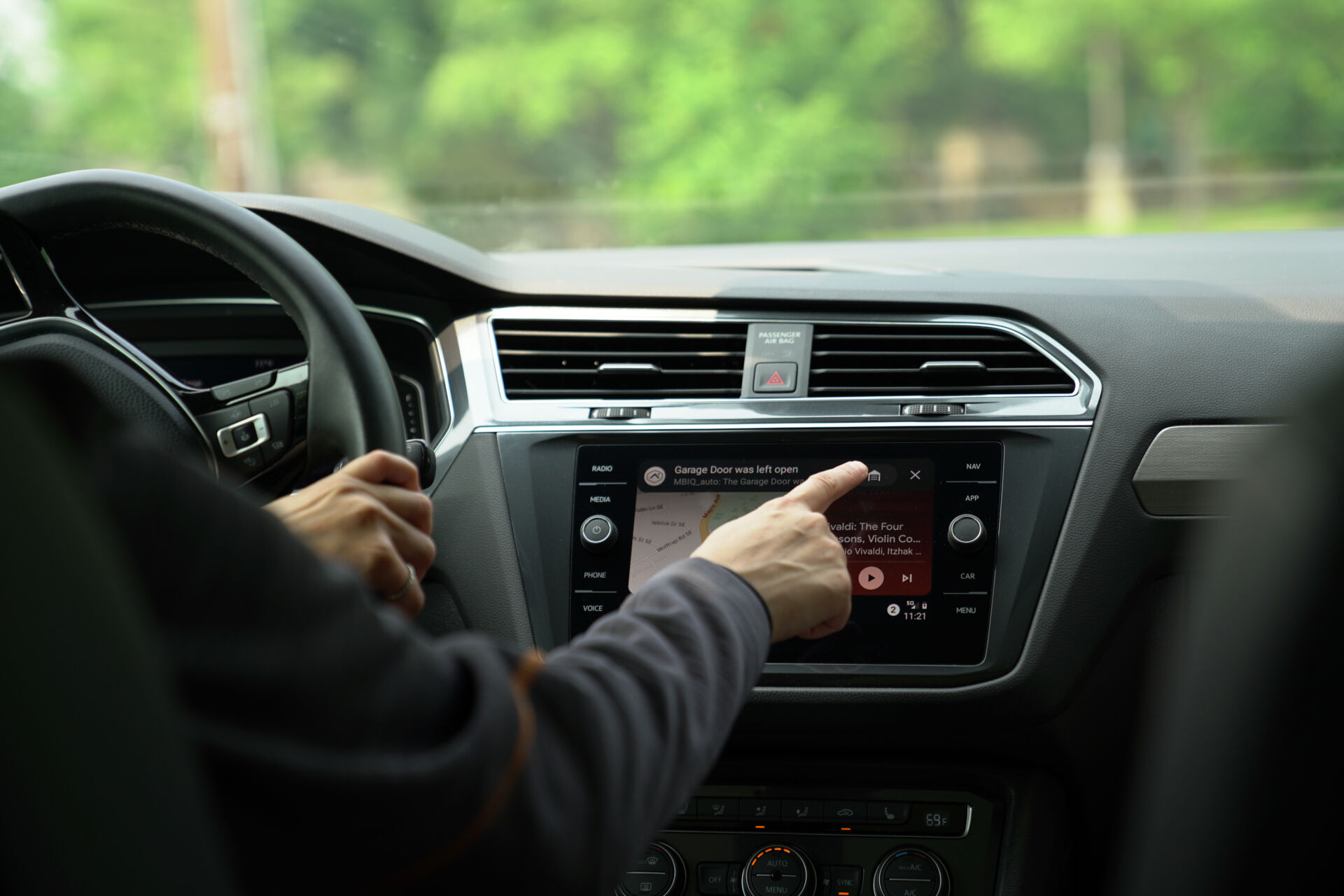Hand reaching toward a car's touchscreen showing a garage door alert
