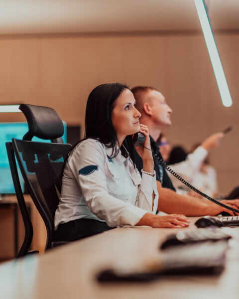 Female security guard operator talking on the phone while working at the workstation with multiple displays Security guards working on multiple monitors. High quality photo