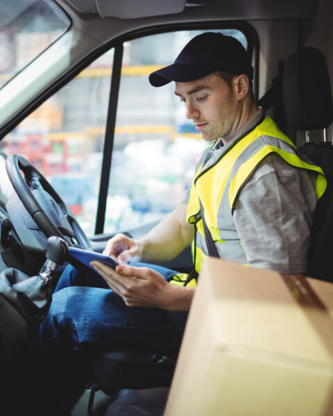 Delivery driver in a high-visibility vest checking a device in his van