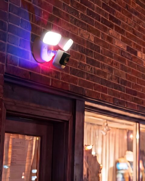 Security camera with an activated floodlight and blue and red warning lights on a brick storefront